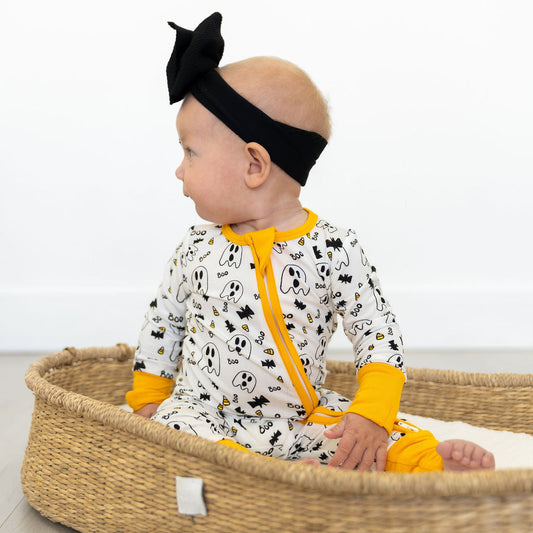 Baby in a crib wearing a black headband and yellow accents, with a white background