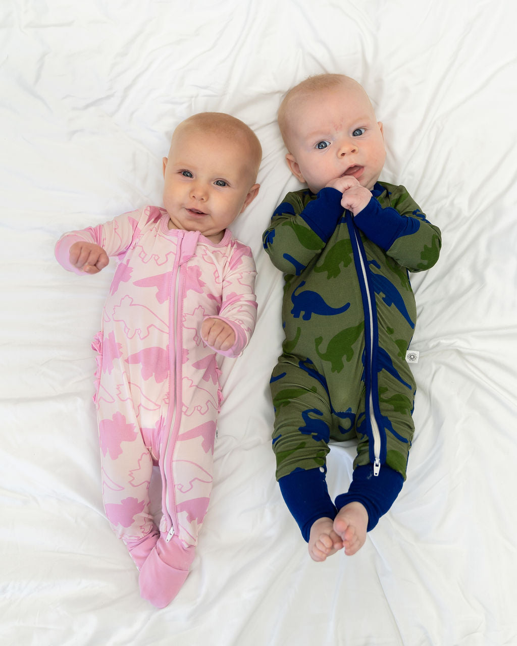Two cute babies wearing a green and pink dinosaur print pajama