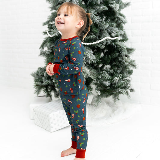 Child wearing a festive pajama set in front of a decorated Christmas tree.