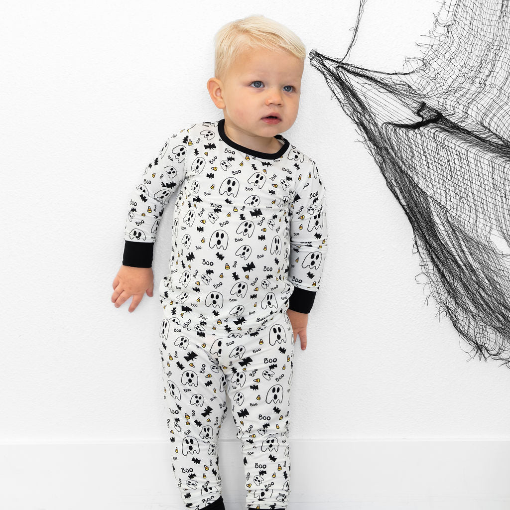 Child wearing a black and white patterned onesie standing next to a fishing net on a white background