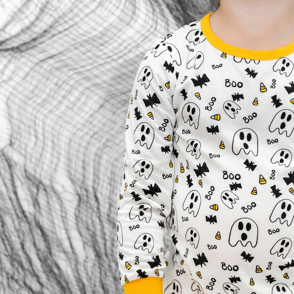 Child wearing a Halloween-themed onesie with ghosts, bats, and candy corn on a white background.