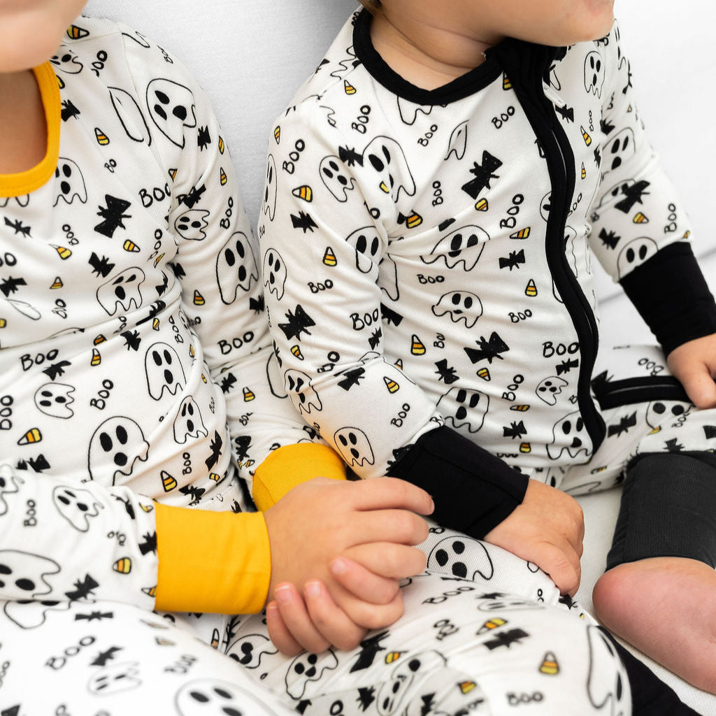 Two children wearing Halloween-themed pajamas with ghost and candy corn designs.