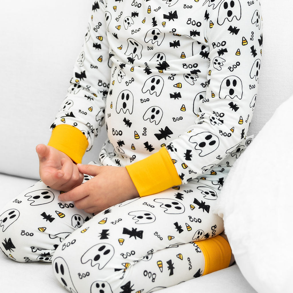 Child wearing Halloween-themed pajamas with ghosts, bats, and candy corn on a white background.