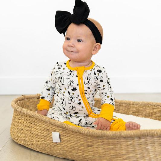 Baby in a wicker crib wearing a black headband and white outfit with yellow accents.